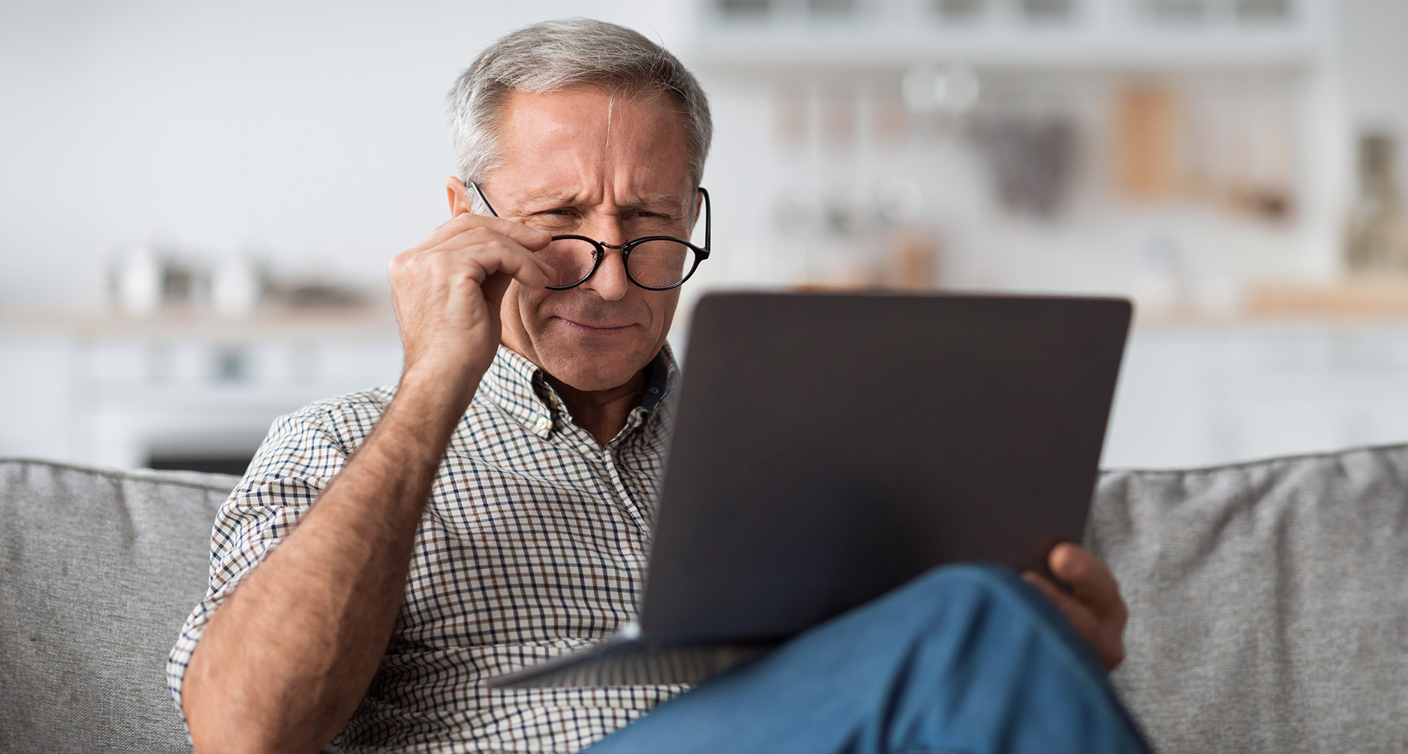 persoană în fața unui laptop purtând ochelari și strâmbând din ochi
